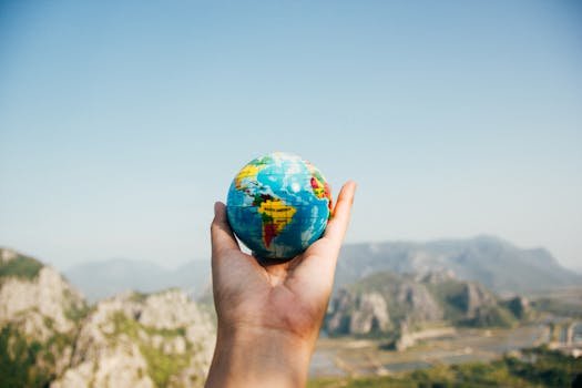 Hand holding a globe against a mountain background symbolizing travel and exploration.